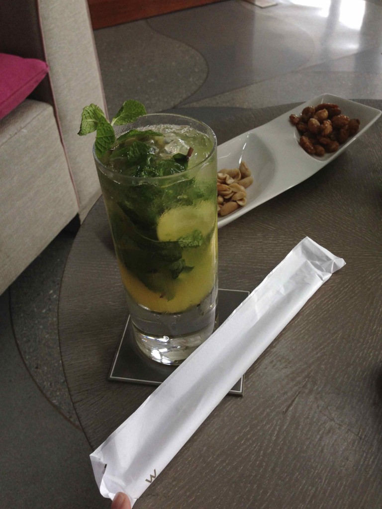 a glass of drink with mint leaves and a plate of nuts