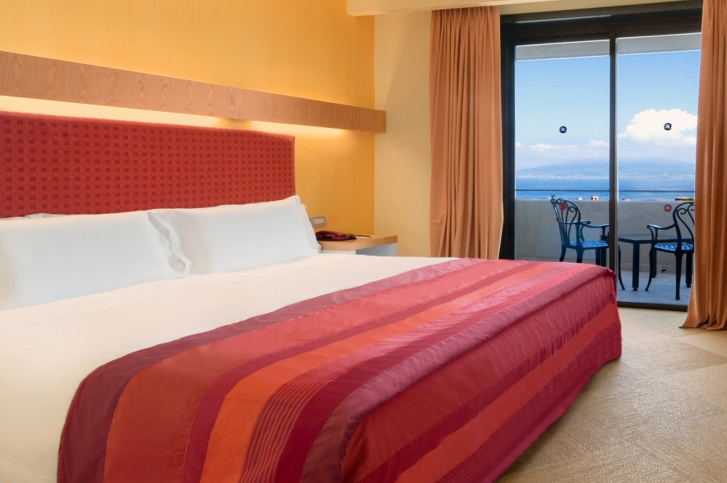 a bed with a red striped bedding and a table and chairs in a room with a view of the ocean