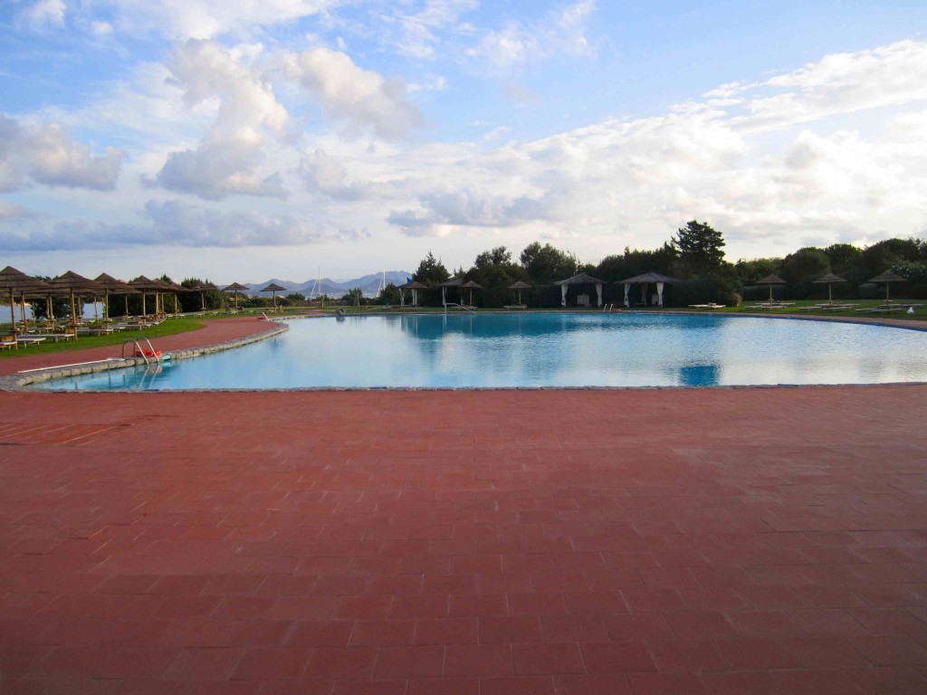 a pool with a red brick walkway and umbrellas