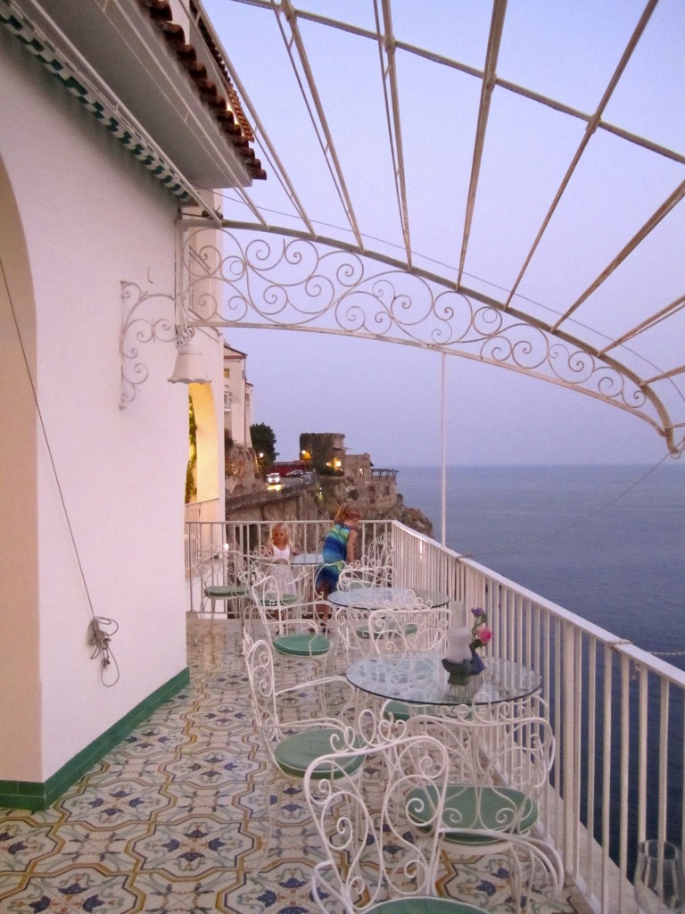 a white patio with tables and chairs on a balcony overlooking the ocean