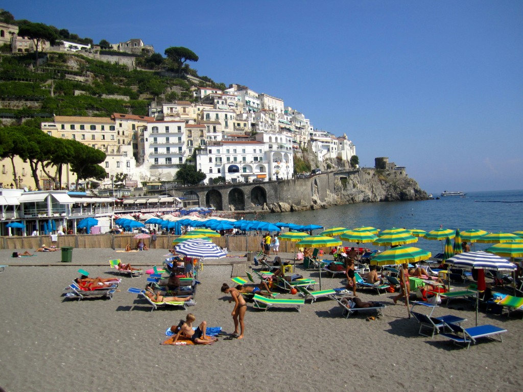 a beach with many chairs and umbrellas and buildings on the side