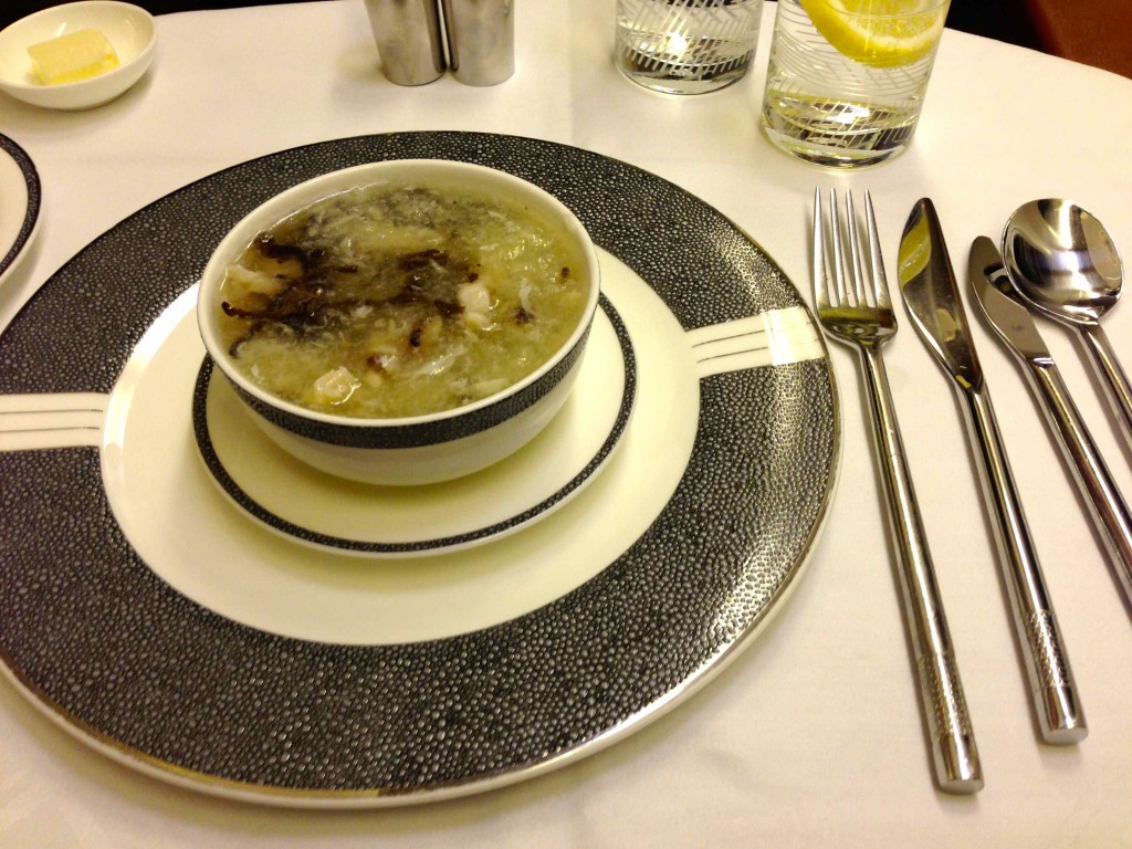 a bowl of soup on a plate with silverware and a fork
