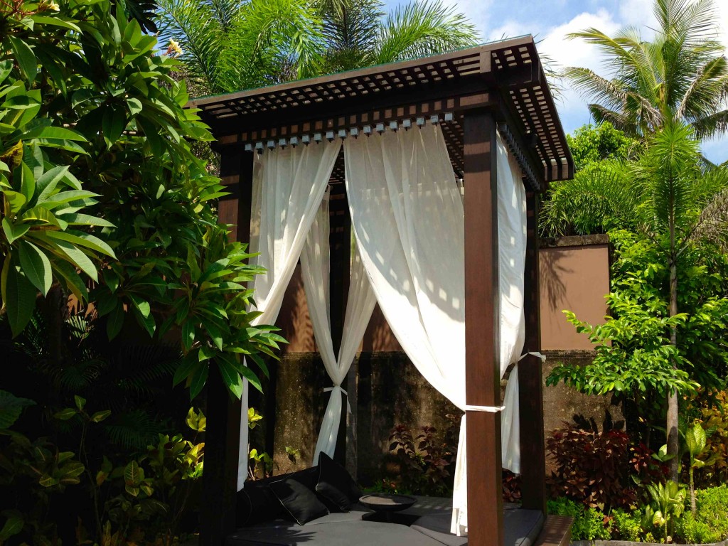 a canopy with white curtains and a bed in a garden