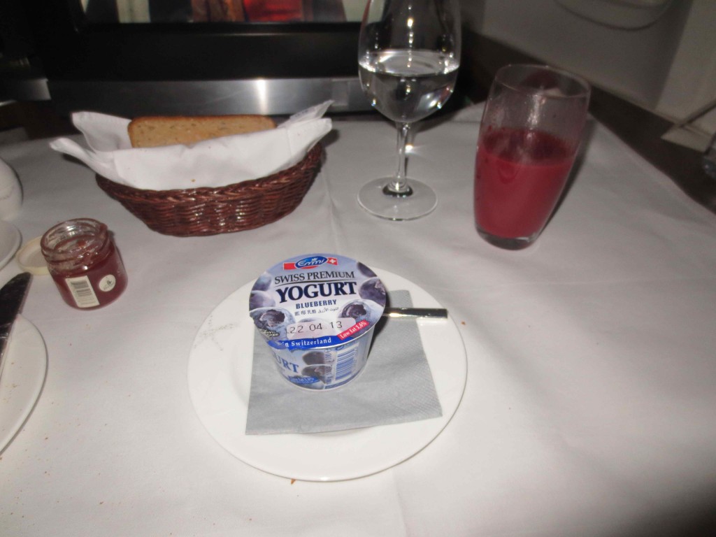 a yogurt on a plate with a glass of juice and a basket of bread