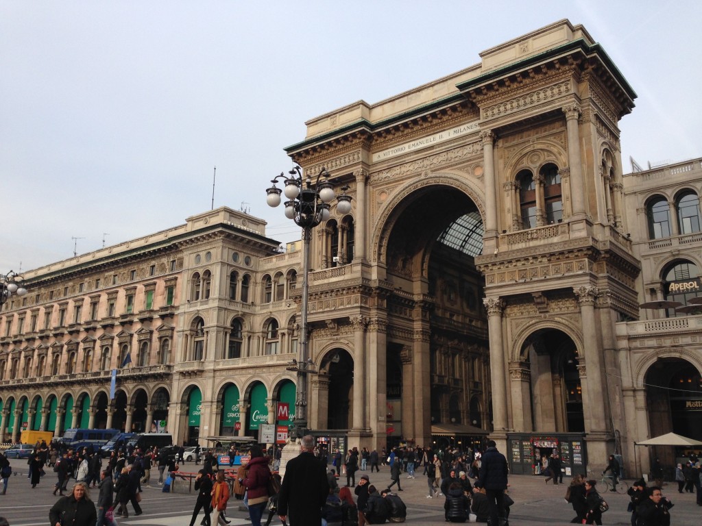 a large stone building with arches and people walking around with Galleria Vittorio Emanuele II in the background