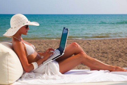 a woman in a garment and hat working on her laptop on the beach