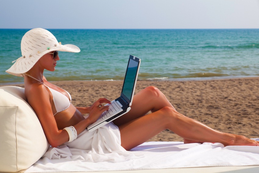 a woman in a garment and hat using a laptop on a beach