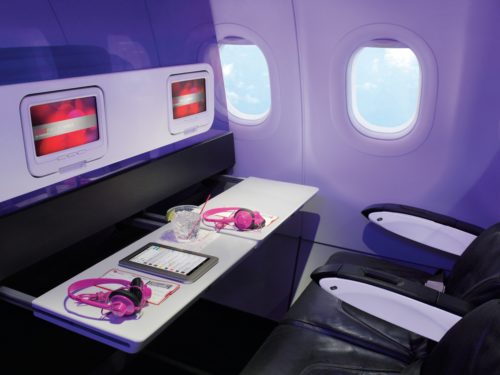 Forget about those obnoxious and filthy armrest tray tables. Virgin built its bulkhead IFE screens and tray tables into a translucent cabin divider. To all other airlines: this is the only acceptable way to do this. (Image courtesy Virgin America)