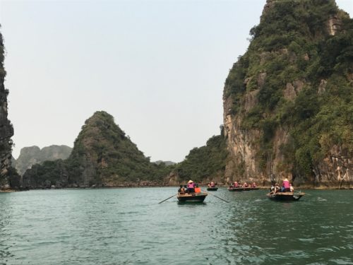 a group of people in boats on water with mountains in the background with Ha Long Bay in the background