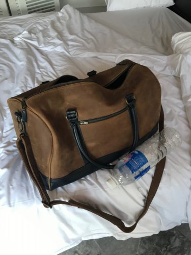 a brown bag with a water bottle on a white bed