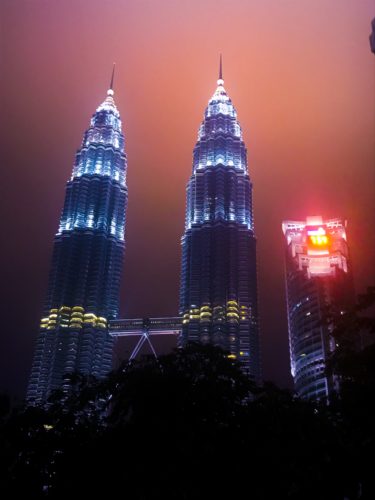 a tall buildings with lights at night with Petronas Towers in the background