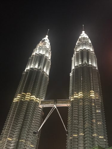 a two towers with lights at night with Petronas Towers in the background