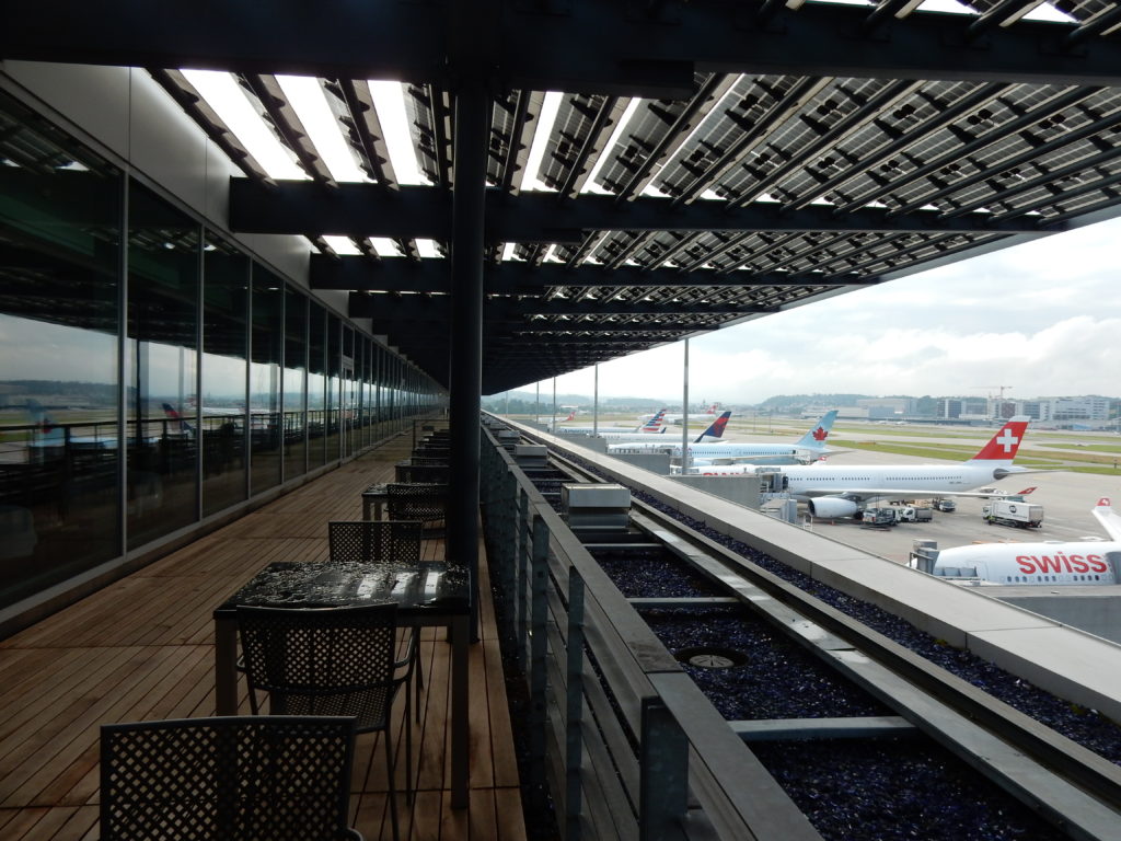 a building with a roof over a walkway with airplanes in the background