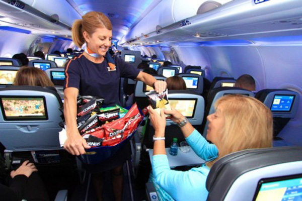 a woman handing a bag of chips to a woman on an airplane
