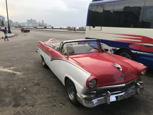 a red and white convertible car parked next to a bus
