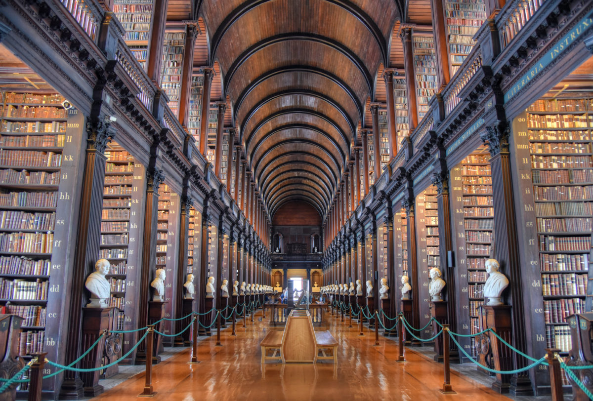 a long library with rows of books and statues with Trinity College Library in the background