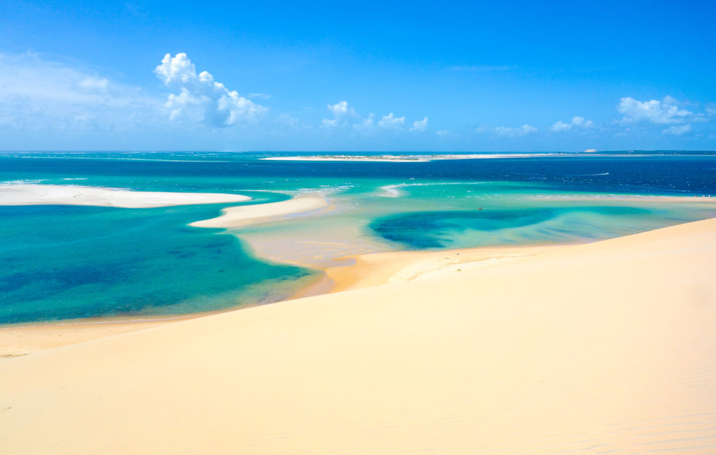 a sandy beach with blue water and blue sky