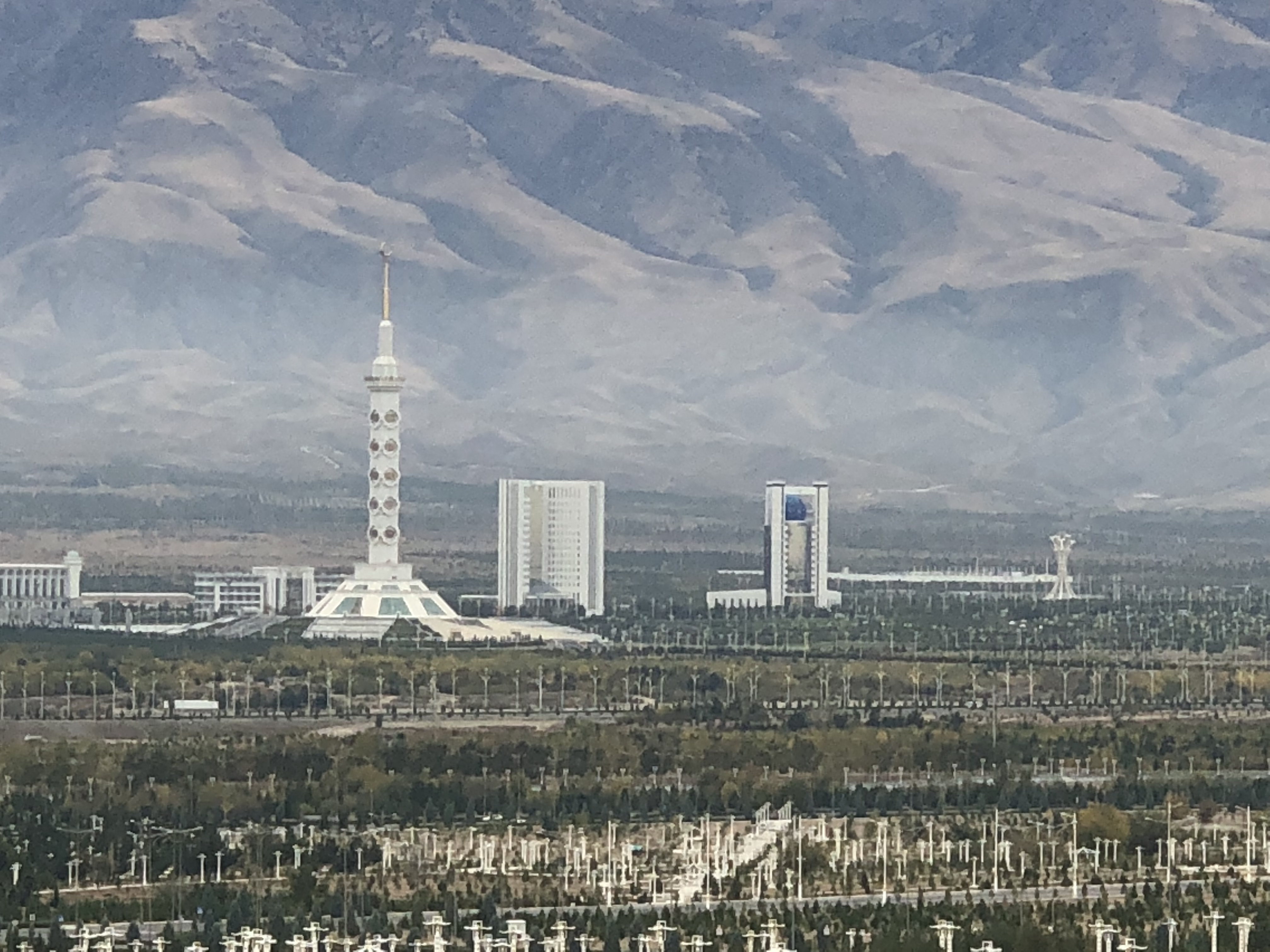 a tall white tower in a city with trees and mountains in the background
