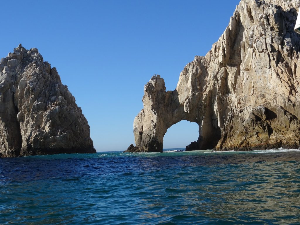 a rock formation in the water with Arch of Cabo San Lucas in the background