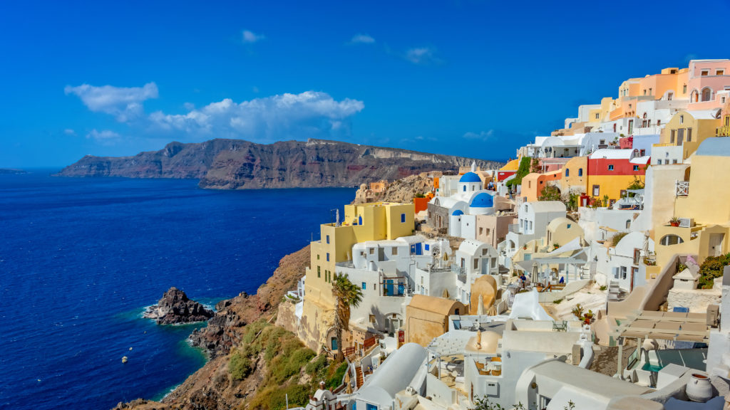 Santorini's iconic white buildings lie on the steep cliffside overlooking the royal blue sea. Oia is known for its sunsets.