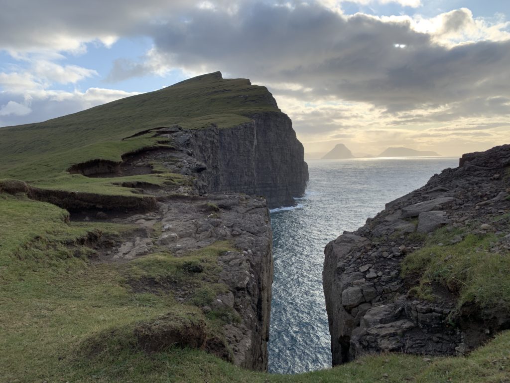 a cliff with a body of water and a grassy hill