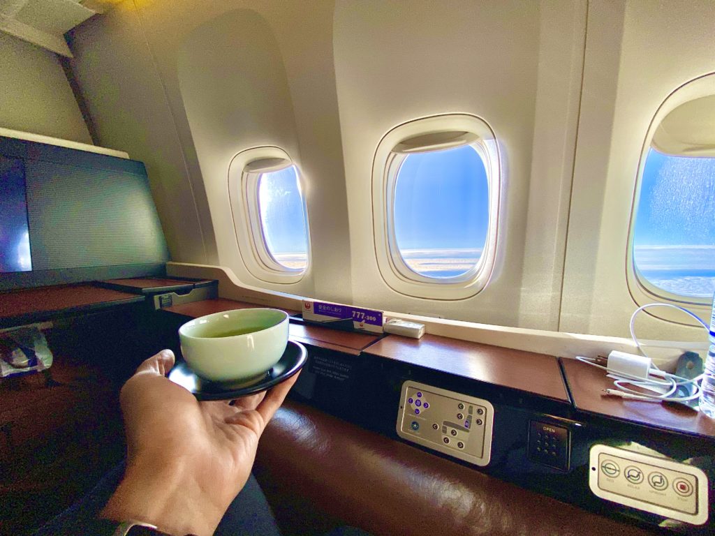 a hand holding a cup and saucer in an airplane