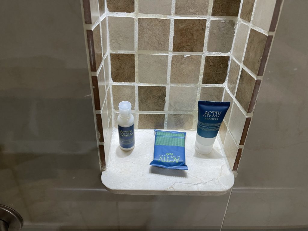 a shower with a tile wall and a small shelf with a small bottle and a small bag